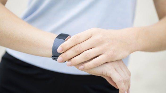 Das Bild zeigt eine Fitness-Uhr am Handgelenk einer Frau.