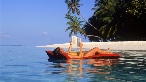 Das Bild zeigt wie eine Frau auf einer Luftmatraze im Meer ein Buch ließt.