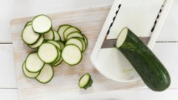 Das Bild zeigt einen Gemüsehobel, auf dem eine Zucchini geschnitten wird.