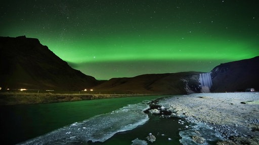 Das Bild zeigt: Polarlichter über dem Wasserfall "Skogafoss".