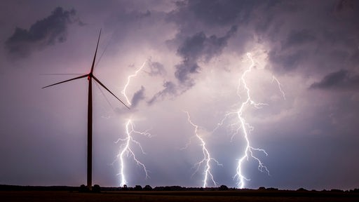 Drei Blitze schlagen auf einem Feld neben einem Windrad ein