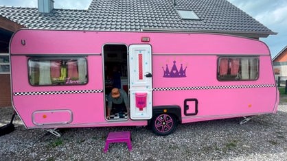 Ein pinker Wohnwagen steht in der Einfahrt eines Hauses. 