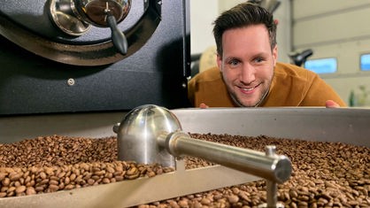 Moderator Sven Kroll schaut zu, wie Kaffeebohnen gemahlen werden.