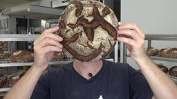 Ein Mann hält sich ein rundes Brot vor das Gesicht
