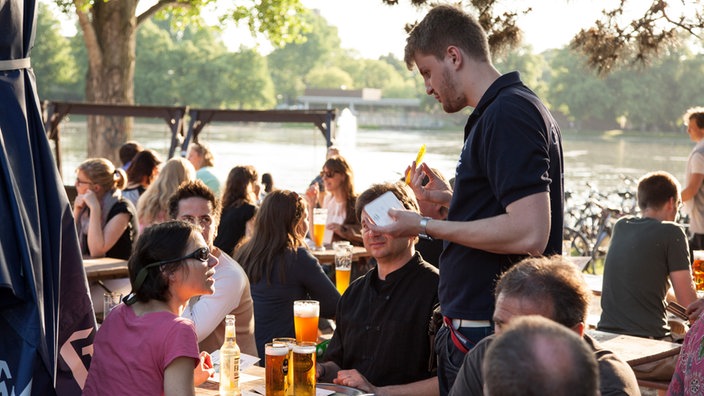 Das Bild zeigt einen Kellner in einem Biergarten.