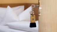 Das Bild zeigt einen Zimmerschlüssel im Türschloss vor einem Bett.