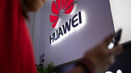 Das Bild zeigt das Huawei Logo, und eine Person, die ein Smartphone hält.