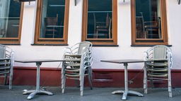 Das Bild zeigt zusammengestellte Tische und Stühle vor einer Gaststätte.