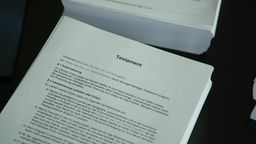 Mehrere Seiten Papier, oben auf liegt ein Dokument mit der Überschrift "Testament"