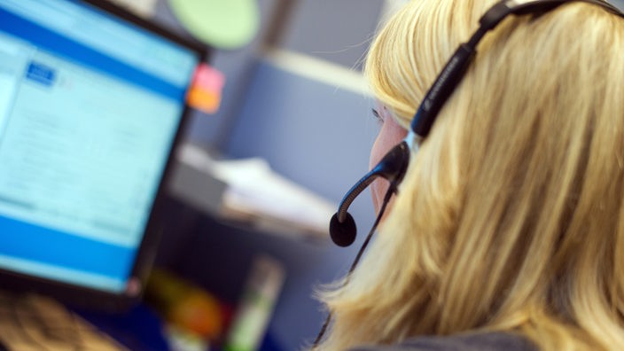 Das Bild zeigt eine Mitarbeiterin eines Callcenters mit einem Headset am Schreibtisch.
