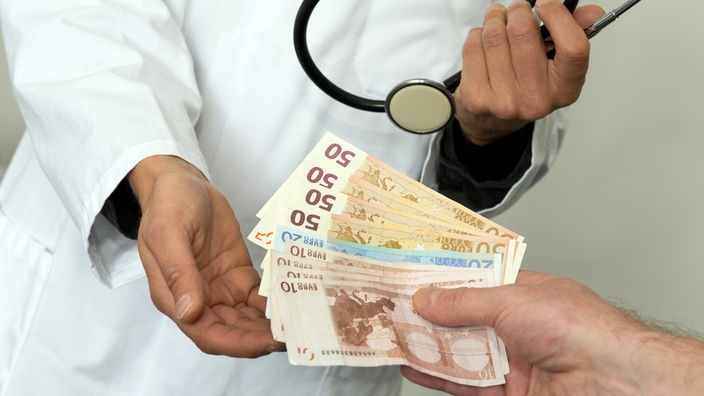 Das Bild zeigt, wie eine Frau in einem Arztkittel Geld annimmt.