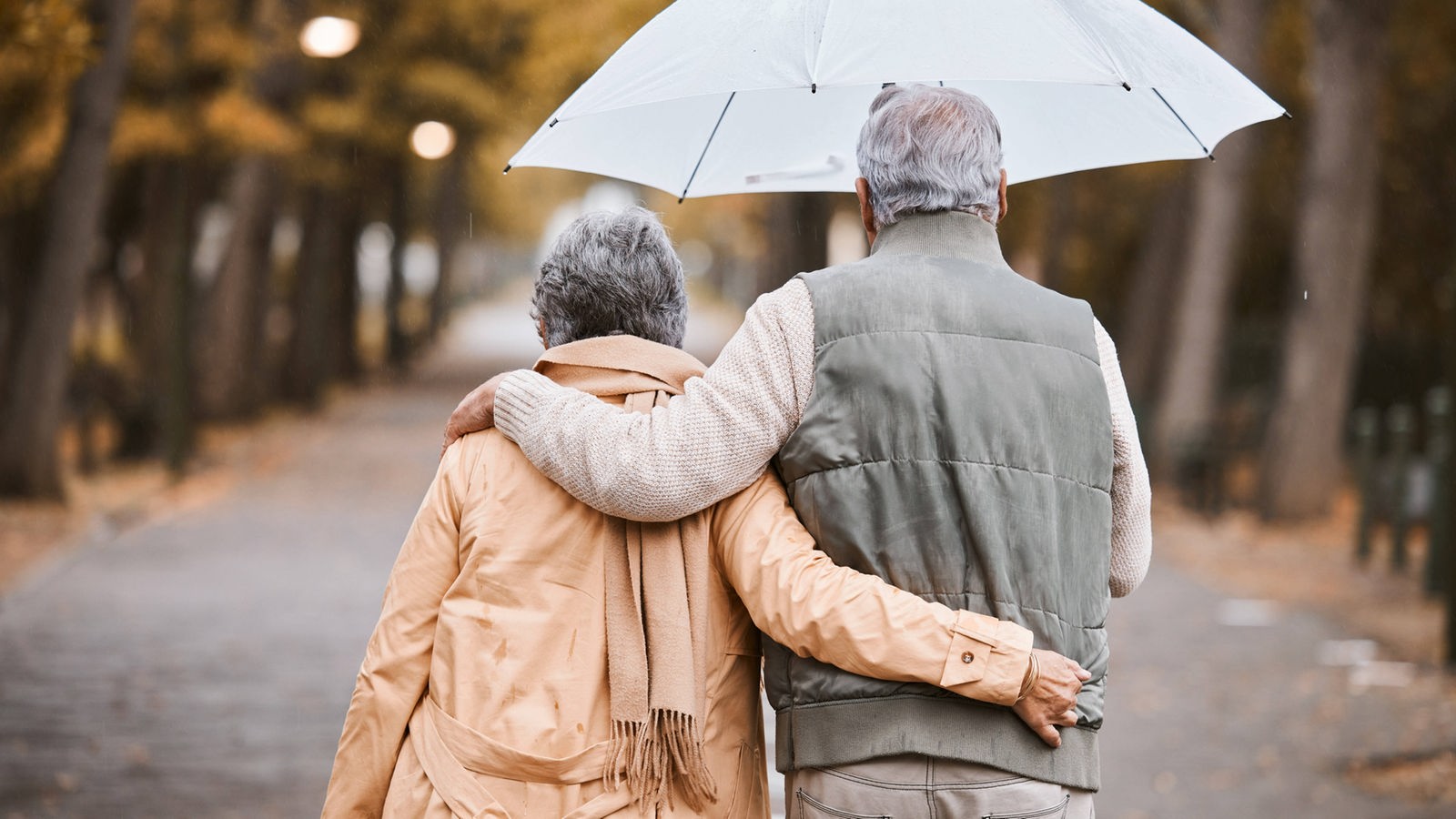 Das Bild zeigt ein älteres Paar mit Regenschirm bei einem Spaziergang im Regen.