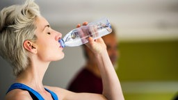 Eine weiblich gelesene Person trink Wasser aus einer Plastikflasche.