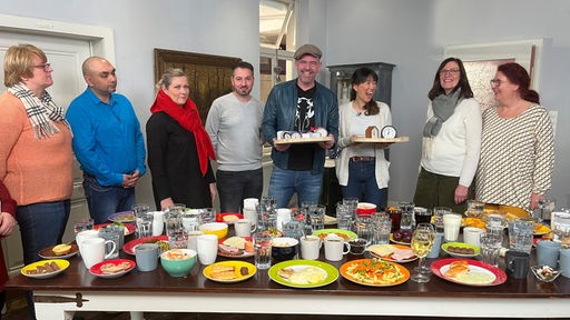 Das Bild zeigt Doc Esser (4. v.r.), Ernährungsexpertin Dr. Jon Chim Bai-Habelski (3. v.r.) mit dem Hospiz-Team an einem Tisch mit Lebenspmitteln.