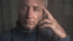 Ein Mann schaut aus seinem Fenster. Es regnet.