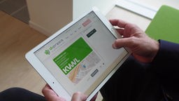 Eine Person hält ein Tablet mit einer Anwendung einer digitalen Praxis geöffnet