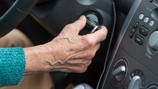 Das Bild zeigt eine ältere Person am Steuer eines Autos.
