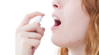 Das Bild zeigt eine junge Frau, die sich ein Spray in den Mund sprüht.