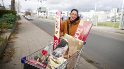 das Bild zeigt eine Frau, die hinter einem Einkaufswagen voller Schokolade steht