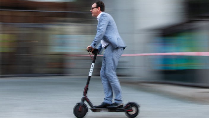 Das Bild zeigt einen Mann auf einem E-Scooter. 