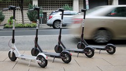 Das Bild zeigt vier E-Scooter am Straßenrand. 