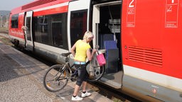 Das Bild zeigt eine Radfahrerin, die in eine Regionalbahn der DB einsteigt.