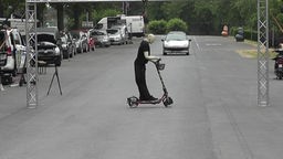 Ein Dummy auf einem E-Scooter. Dahinter ein heranfahrendes Auto