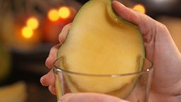 Das Bild zeigt wie man Mangofleisch am Rand eines Glases löst.
