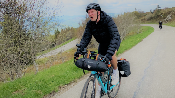 Moderator Christian Loß fährt sichtlich angestrengt bergauf Fahrrad.