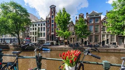 Ein Fahrrad mit Tulpen steht an einem Kanal in Amsterdam.