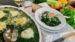 Spinatauflauf mit versunkenen Eiern in einer Ofenform sowie eine Portion auf einem Teller angerichtet