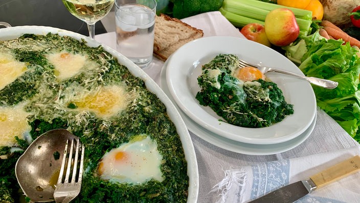 Spinatauflauf mit versunkenen Eiern in einer Ofenform sowie eine Portion auf einem Teller angerichtet