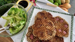 Speckendicken - Waffeln mit Speckscheiben auf einer Platte angerichtet, daneben eine Schüssel mit grünem Salat