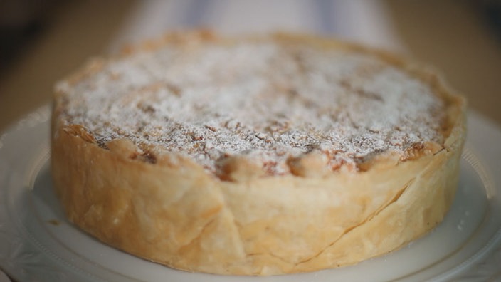 Hellbrauner, runder Kuchen mit Puderzucker bestreut, auf einer Kuchenplatte