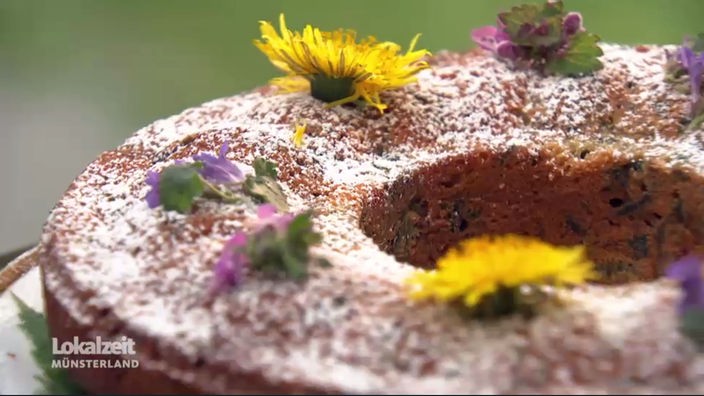 Ein runder Topfkuchen mit Puderzucker und verschiedenen Wildblüten zur Deko