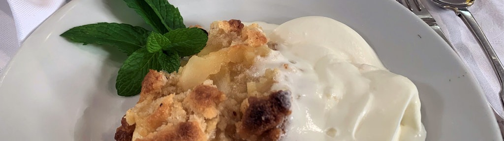 Portion Apfelstreusel mit Sahne auf einem Teller 