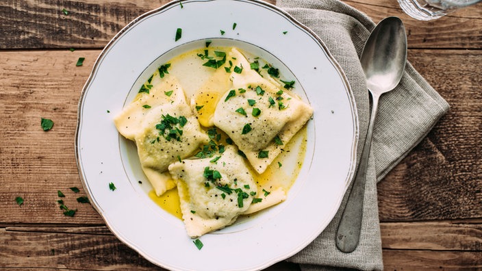 Das Bild zeigt Maultaschen auf einem Teller mit Butter und Kräutern.