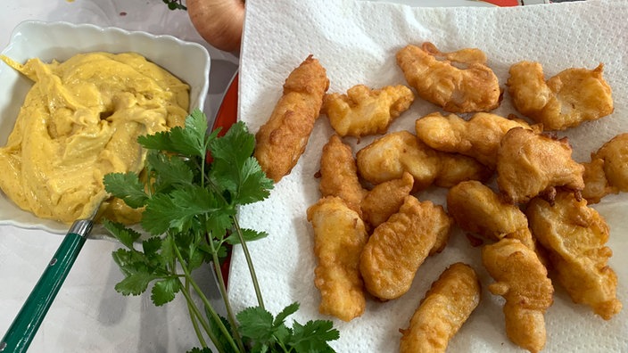 Gebackene Kibbeling auf einem Küchenpapier, daneben in einer Schale Curry-Mayonnaise