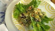 Oktopus mit Couscous und Petersilie auf grünem Blattsalat auf einem Teller angerichtet