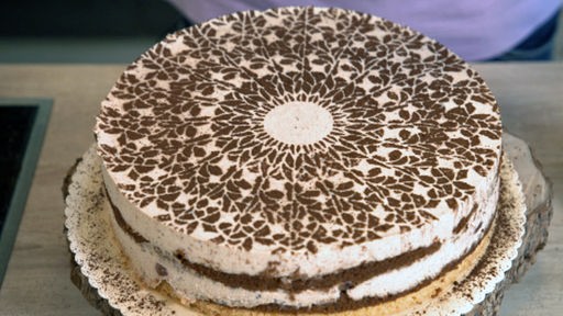 Die mit Backkakao verzierte braun weiße Pflaumen-Joghurt-Torte auf einem Kuchenteller