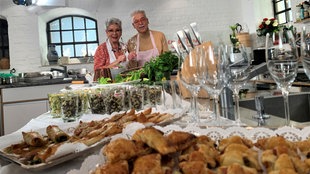 Martina und Moritz stehen hinter einem Tisch mit Häppchen und Tapas für das Silvesterbuffet