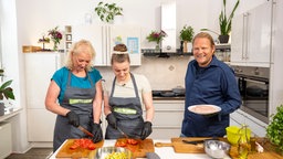  Björn Freitag (r.) mit Pfanne und zwei Mitarbeiter der Jugendhilfe im Hintergrund.