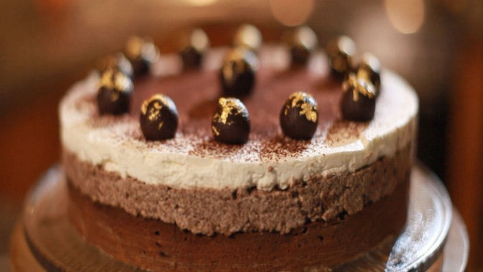 Torte mit  2 verschiedenen braunem Böden, darüber Sahneschicht, darüber dunkle Marzipankugeln mit Blattgold