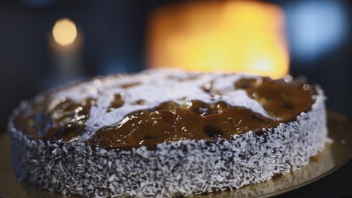 Auf einem großen Teller liegt ein Kuchen. Der Rand des Kuchens ist mit Kokosraspeln bestreut und auf der Oberfläche befindet sich ein großer Stern aus Puderzucker.