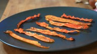 Das Bild zeigt mehrere Streifen Carrot Bacon angerichtet auf einem Teller.