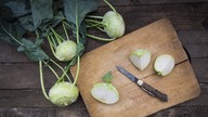 Ein Kohlrabi wird auf einem Holzbrett in Viertel geschnitten.