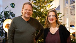 Björn Freitag und Yvonne Willicks stehen vor einem geschmückten Weihnachtsbaum.