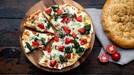 Das Bild zeigt selbstgemachte Fladenbrot-Pizza mit Spinat und Tomaten.