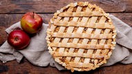 Das Bild zeigt gedeckten Apfelkuchen und Äpfel auf einem Küchentuch.
