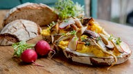 Käse-Rührei mit Pilzen auf einer Scheibe Brot mit dünnen Scheiben Radieschen.
